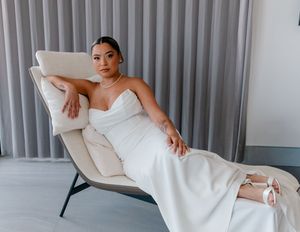 Bride in elegant white strapless mermaid gown reclines gracefully on a modern chaise lounge chair.