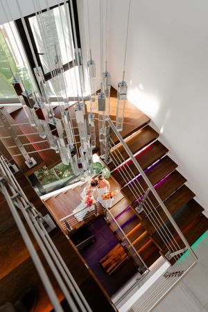 Aerial view of elegant wooden staircase with modern chandelier and two people descending in a luxury interior.