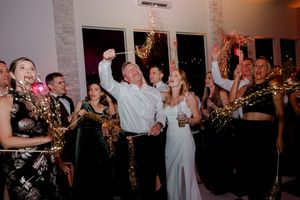 Wedding guests celebrate with sparklers at a festive indoor reception, smiling and taking a selfie together.