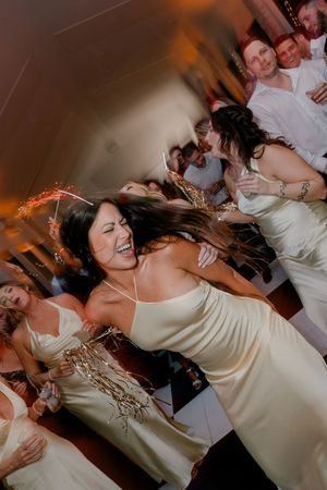 Bridesmaids in gold dresses dancing and laughing joyfully at a wedding reception party.