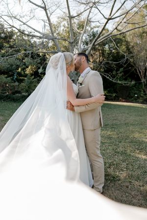 A romantic wedding moment captured outdoors with a flowing white dress and beige suit against a natural garden backdrop.