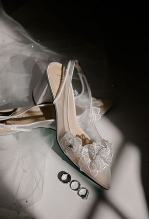 Elegant white lace wedding shoes and wedding rings arranged artistically with soft shadows.