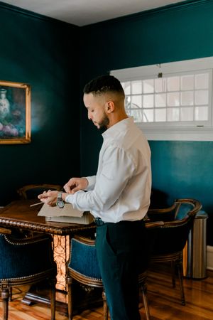 A person in a white shirt sits at a wooden desk in a room with dark teal walls and natural lighting.