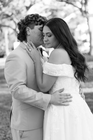 A romantic wedding couple embraces and kisses in a black and white outdoor photo series.