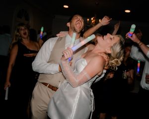 Bride and groom dancing joyfully with glowing light sticks at their wedding reception party.
