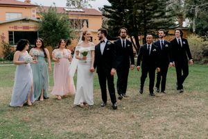 Wedding party in formal attire walks together on grassy lawn during outdoor celebration.