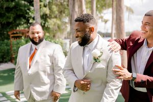 A group of people in white formal attire laughing and celebrating together at an outdoor event.