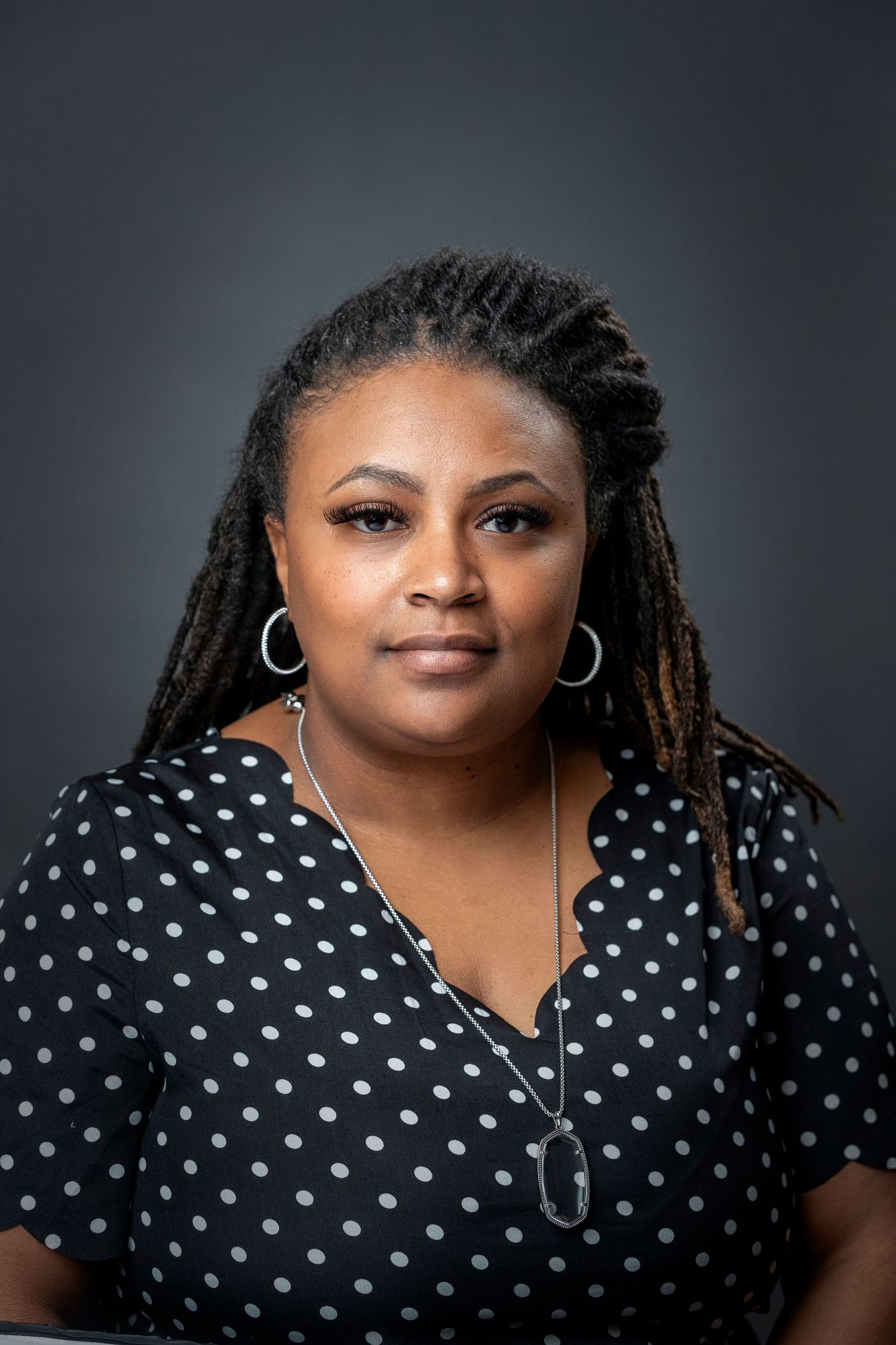 Professional studio portrait of person wearing polka dot top against dark background.