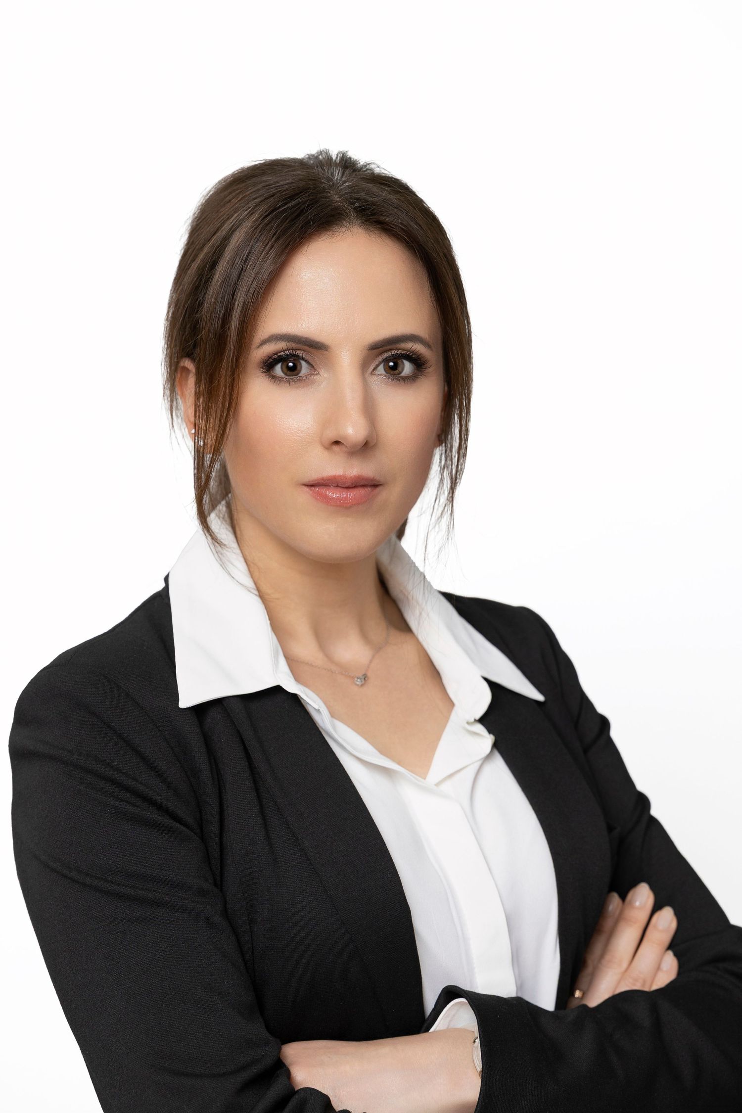 Professional wearing black blazer and white collared shirt poses with crossed arms in studio setting.