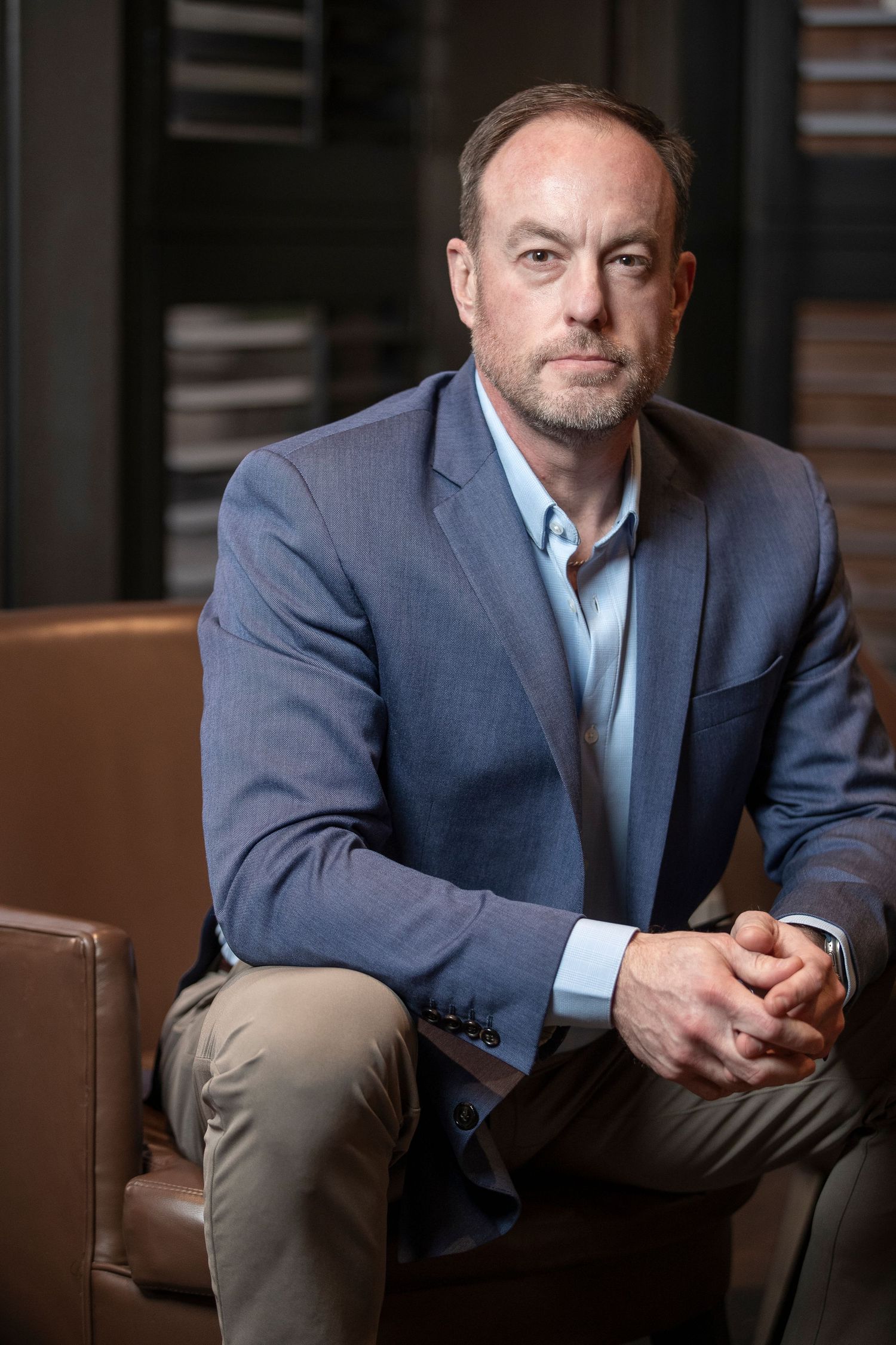 Professional portrait series of businessman in blue blazer sitting on leather chair in corporate setting.