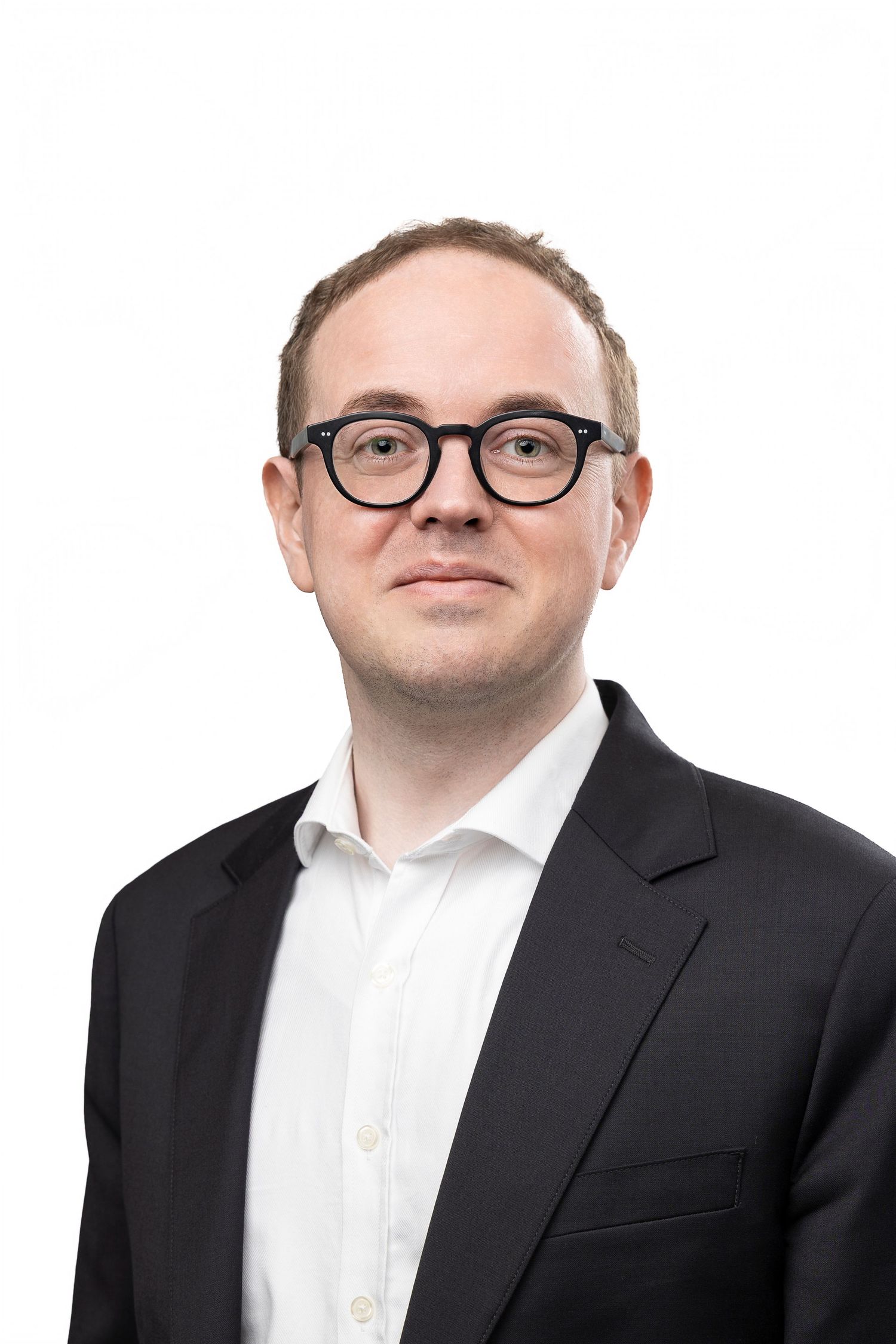 Professional headshot of a young man wearing black-rimmed glasses and a dark blazer with white shirt on white background.