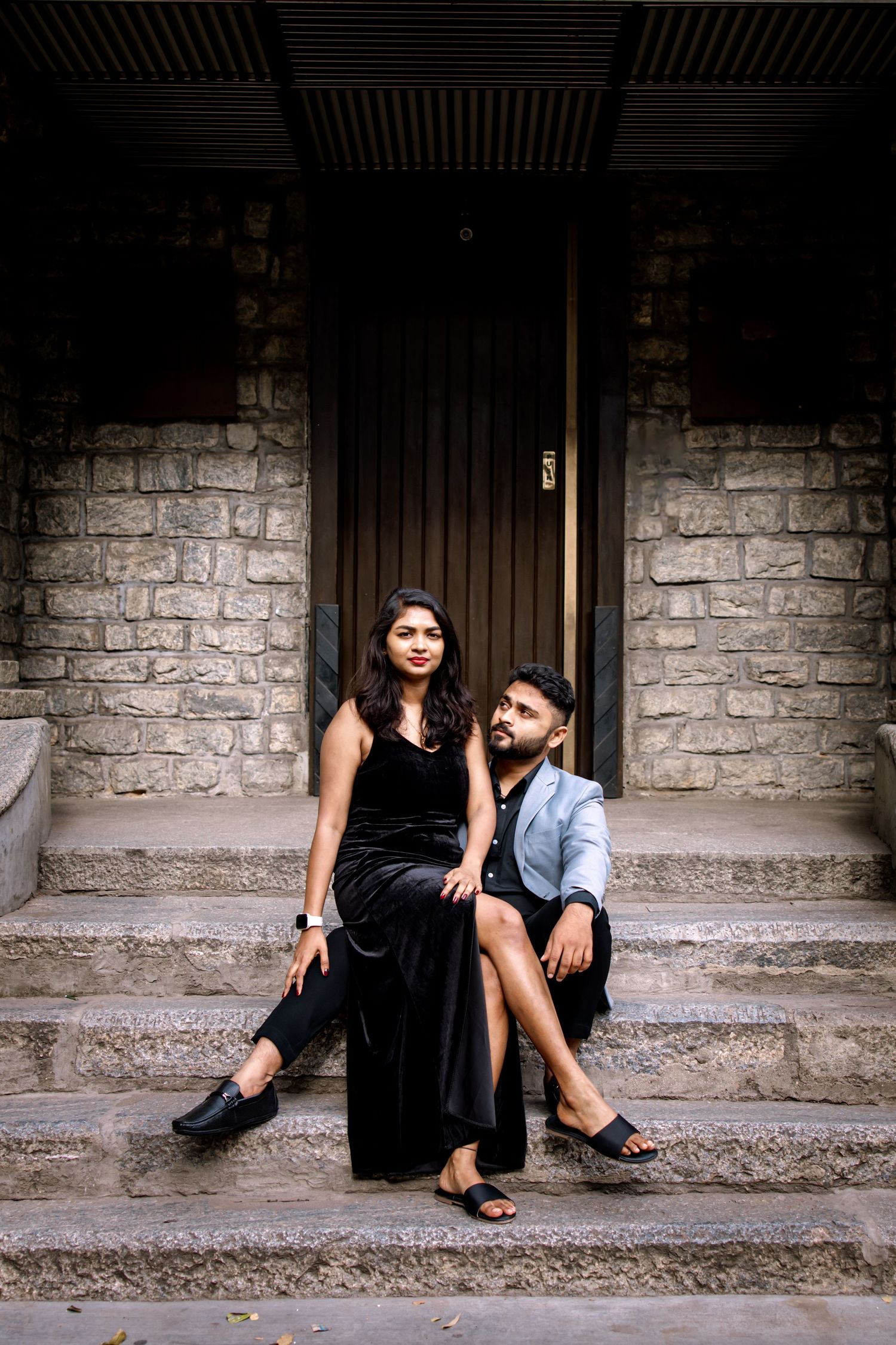 Two people in casual attire sitting on stone steps against a brick wall.