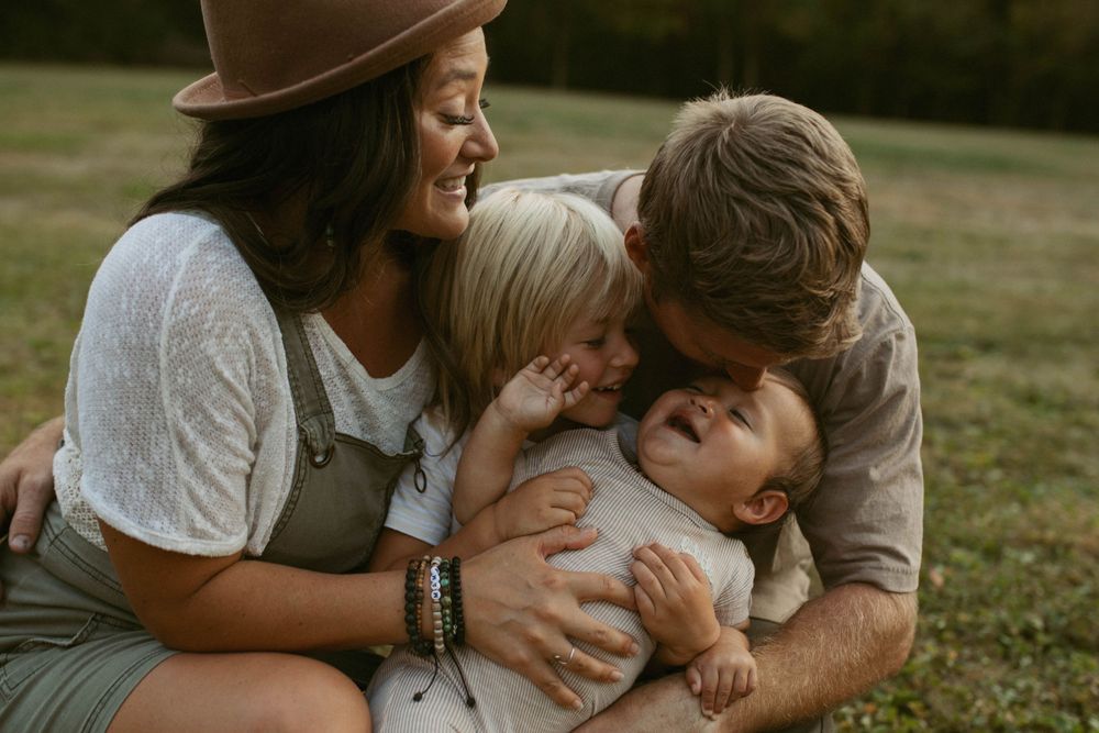 Loving family of four sharing a joyful embrace outdoors on a green lawn during golden hour.