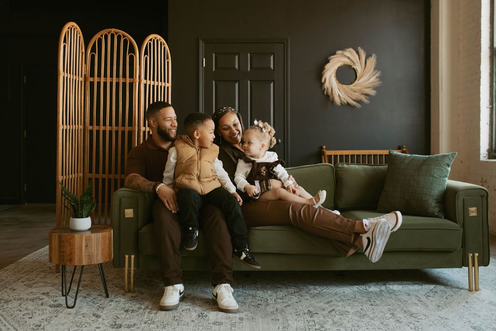 A happy family of four poses together on a green couch in a stylish dark-themed living room.