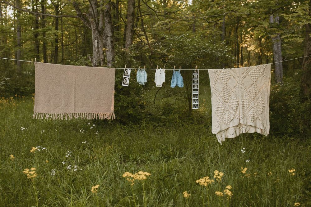Baby clothes and blankets hang on a clothesline in a sunny meadow surrounded by wildflowers.