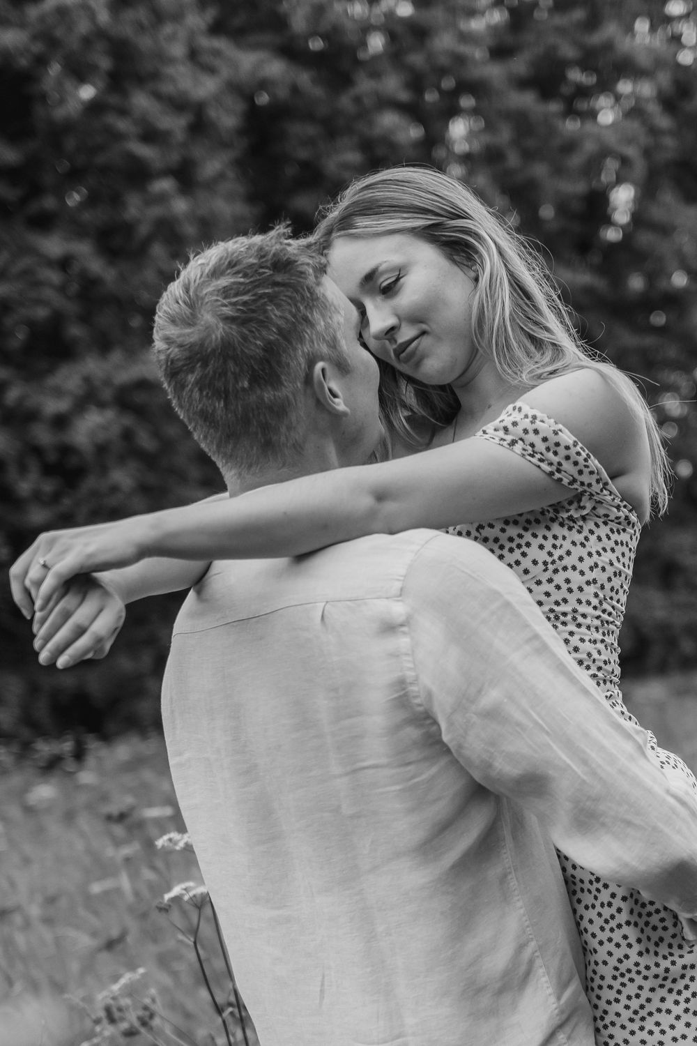 A romantic black and white photo of a couple embracing outdoors, sharing an intimate moment together in a natural setting.
