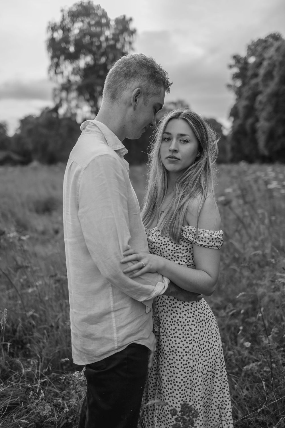 A couple in monochrome embraces affectionately in a wildflower field wearing casual summer attire.