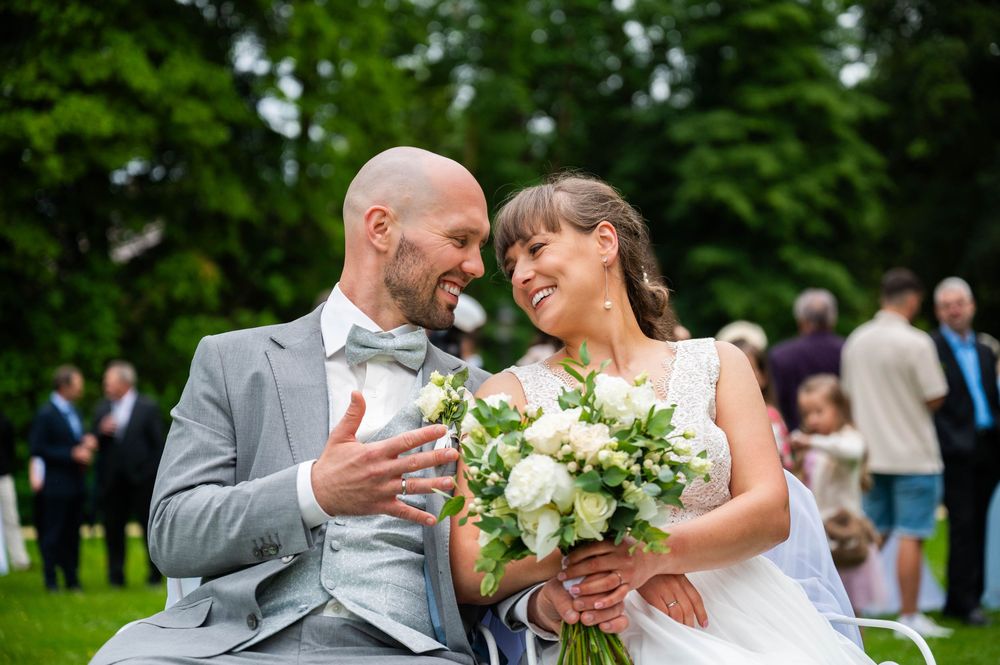 Bride and groom sharing a joyful moment while holding white floral bouquet during outdoor garden wedding celebration.
