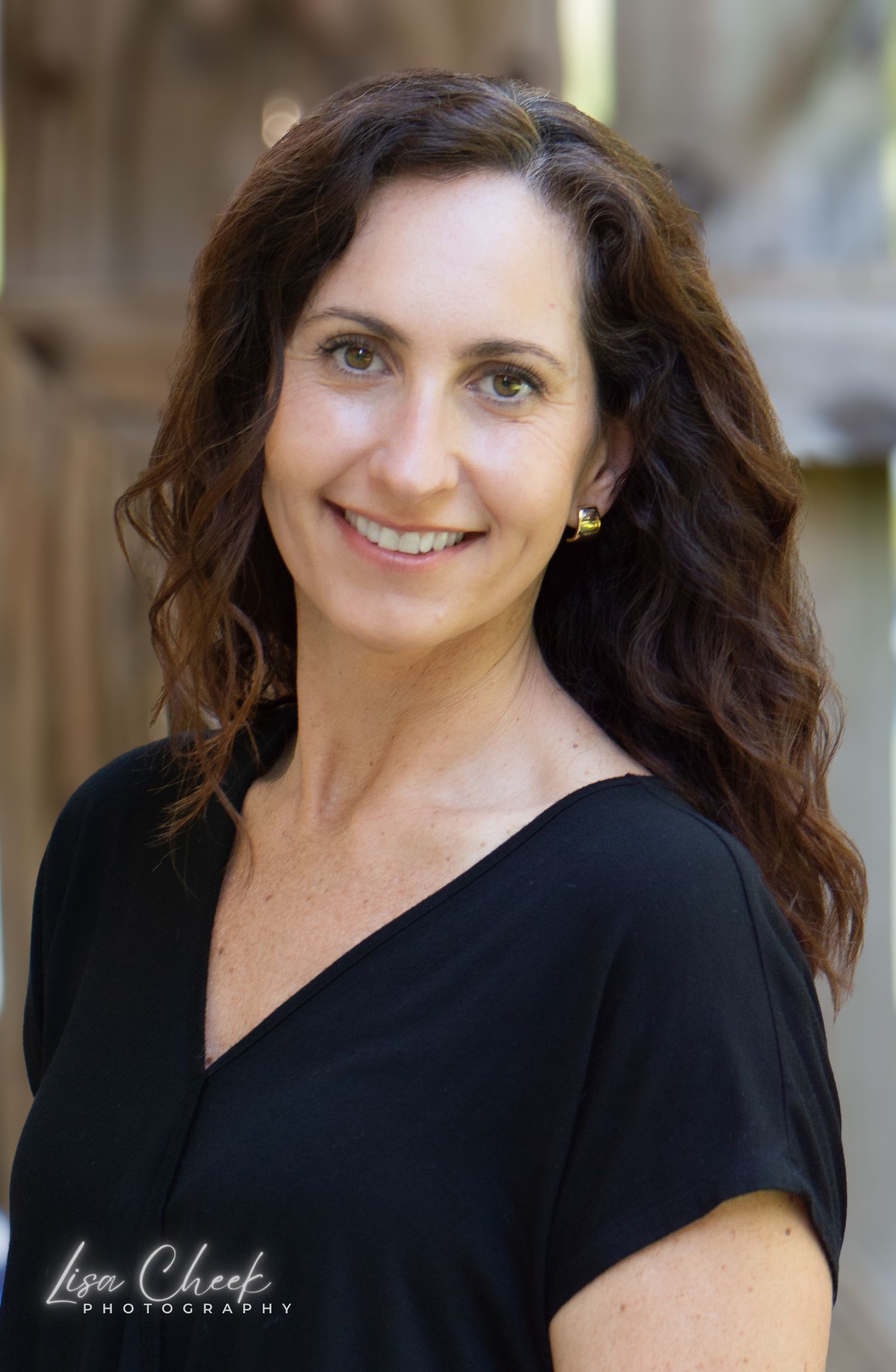 A  professional headshot photos showing someone wearing a black top against a blurred background.