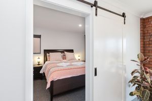 Modern bedroom interior with dark wood bed frame, sliding barn door, exposed brick wall, and natural light.
