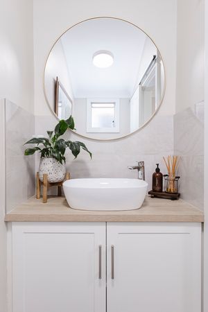 Modern white bathroom interior with round mirrors, vessel sink, and wooden countertop on white cabinets.