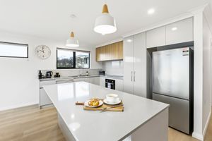 Modern white kitchen with island bench, pendant lights, stainless steel fridge, and timber accents in a bright open plan.