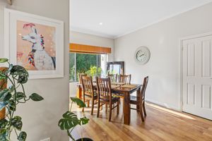 Bright dining room with hardwood floors, wooden table and chairs, wall clock, and colorful giraffe artwork near a sunlit window.