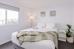 Bright white bedroom with green striped throw blanket, floor lamp, bedside table, and indoor plant near window.