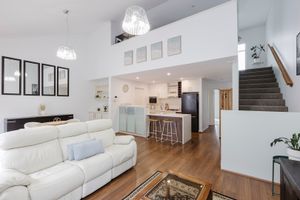 Modern open-concept living room with white leather sofa, hardwood floors, kitchen island, and double-height ceilings.