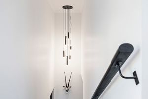 Modern black pendant lights cascade down a bright white stairwell with sleek black handrail.