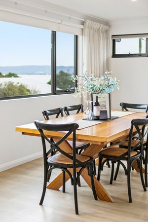 Modern dining room with wooden table, black cross-back chairs, floral centerpiece, and large windows overlooking a scenic view.