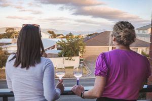 Two people enjoying wine on a balcony overlooking a suburban neighborhood at sunset.