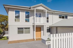 Modern two-story home with white weatherboard exterior, timber front door, balcony, and white picket fence at 179.