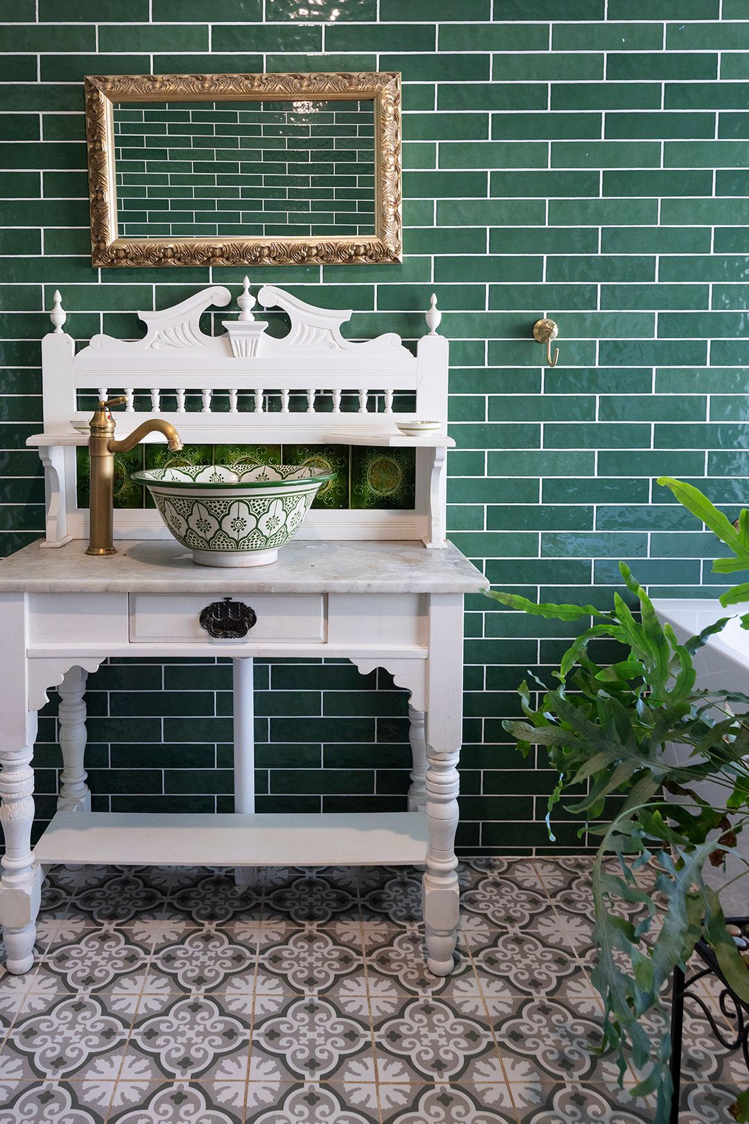 Vintage white washstand with green Moroccan bowl sink against emerald subway tiles, gold faucet, ornate mirror frame.