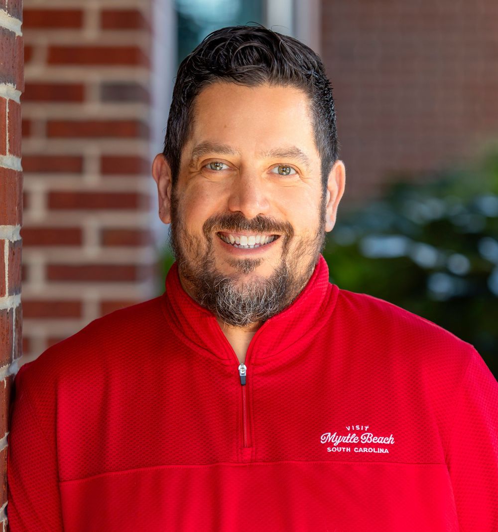 Professional headshot of a man against a brick wall.