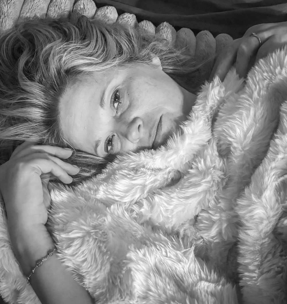 Black and white portrait of a woman lying on a fluffy blanket, gazing at the camera.