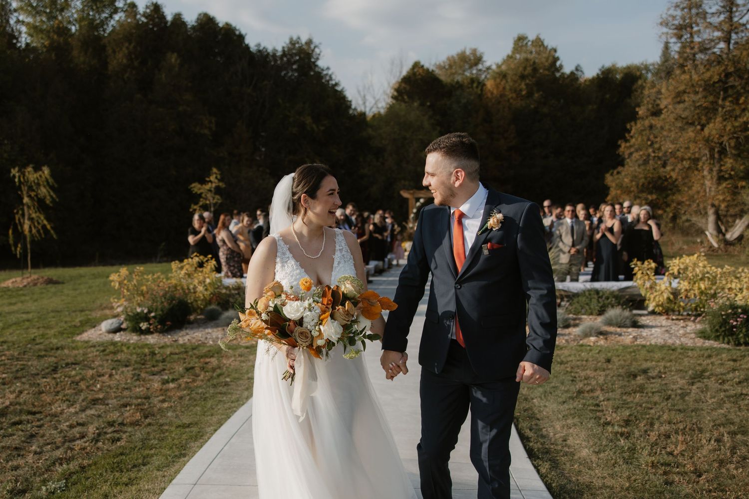 Wedding bouquet featuring deep burgundy and white flowers against a dramatic sunset backdrop.
