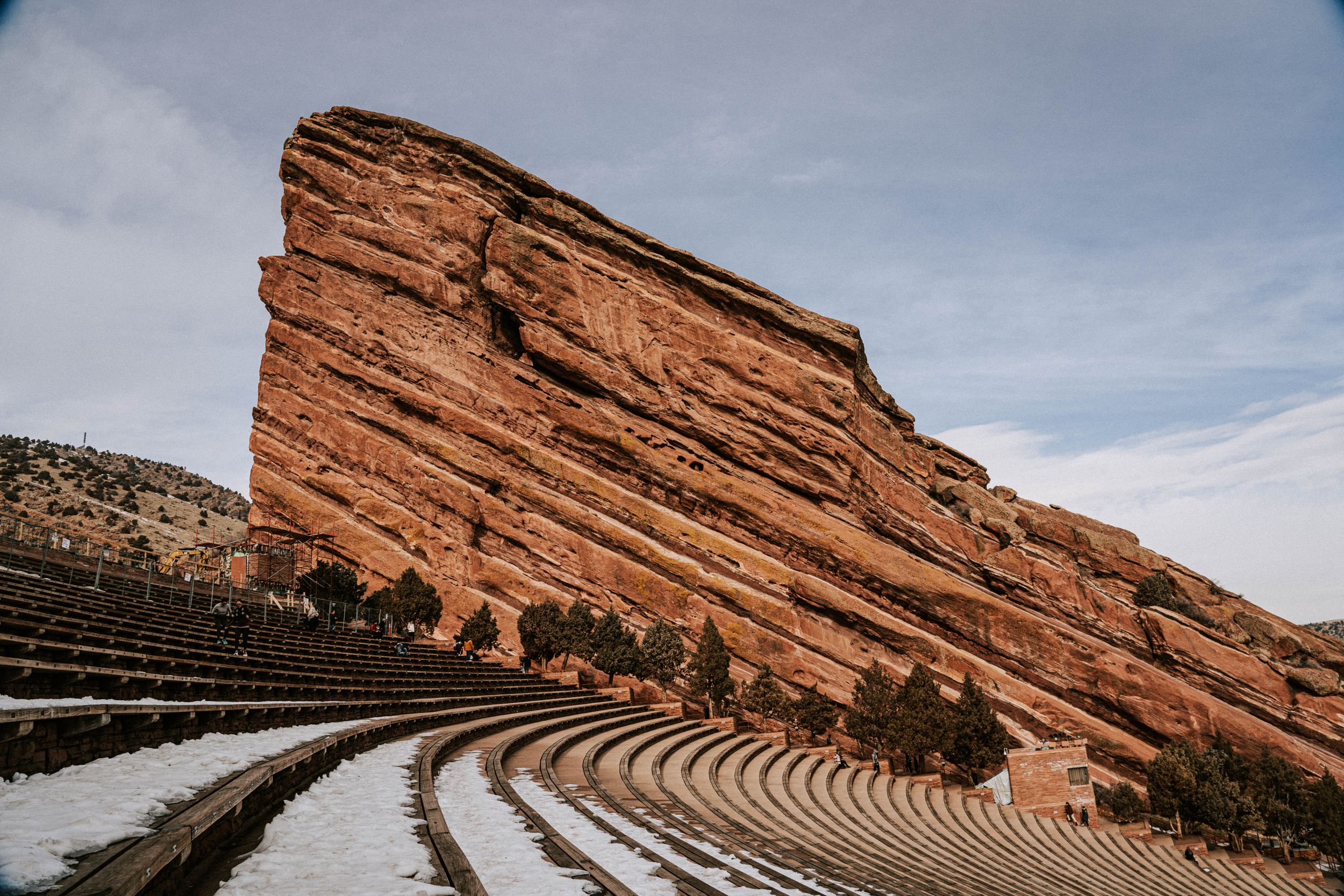 Red rock amphitheater with curved seating rows covered in snow against cloudy sky.