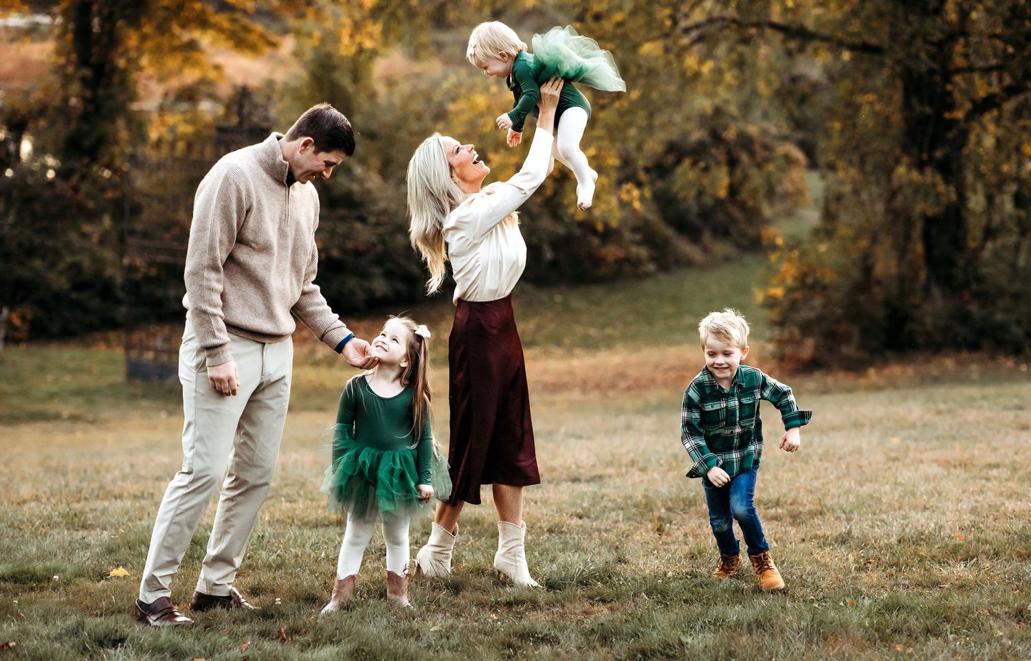 Happy family plays together in autumn foliage at park on sunny afternoon.