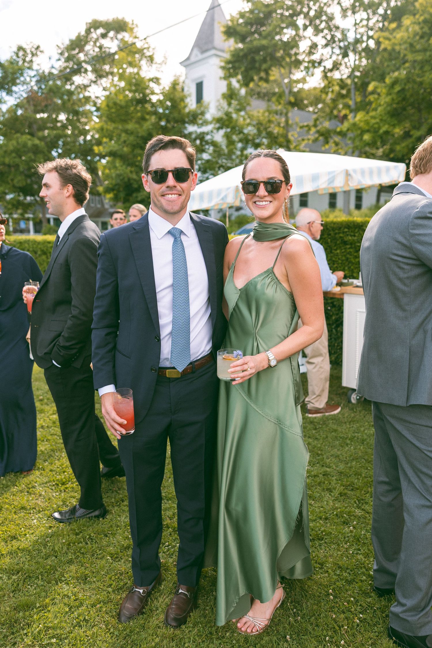 Couple in formal attire, man in navy suit and woman in green slip dress, posing at outdoor wedding reception.