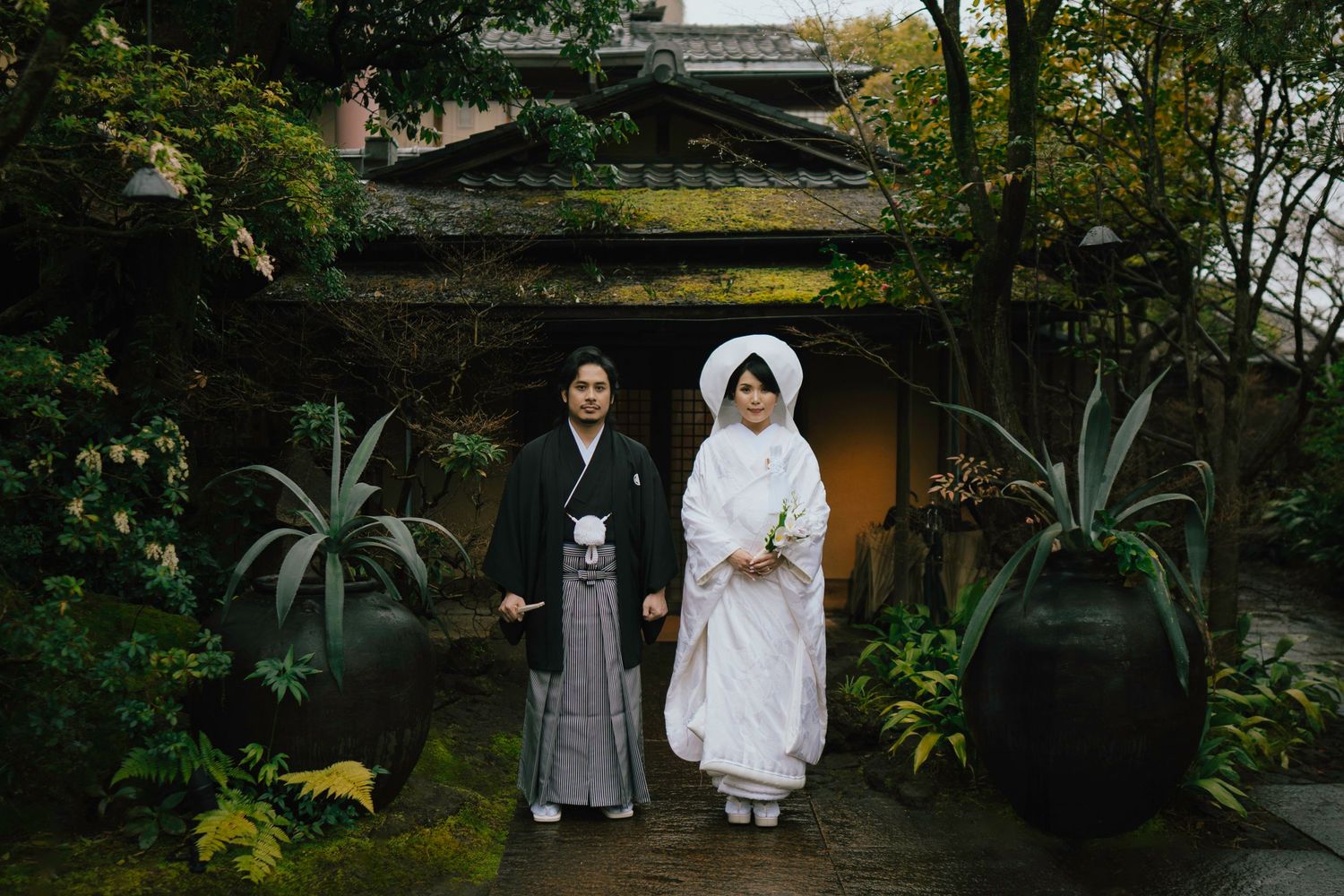 Traditional Japanese wedding couple in kimono and shiromuku standing in a serene garden pathway.