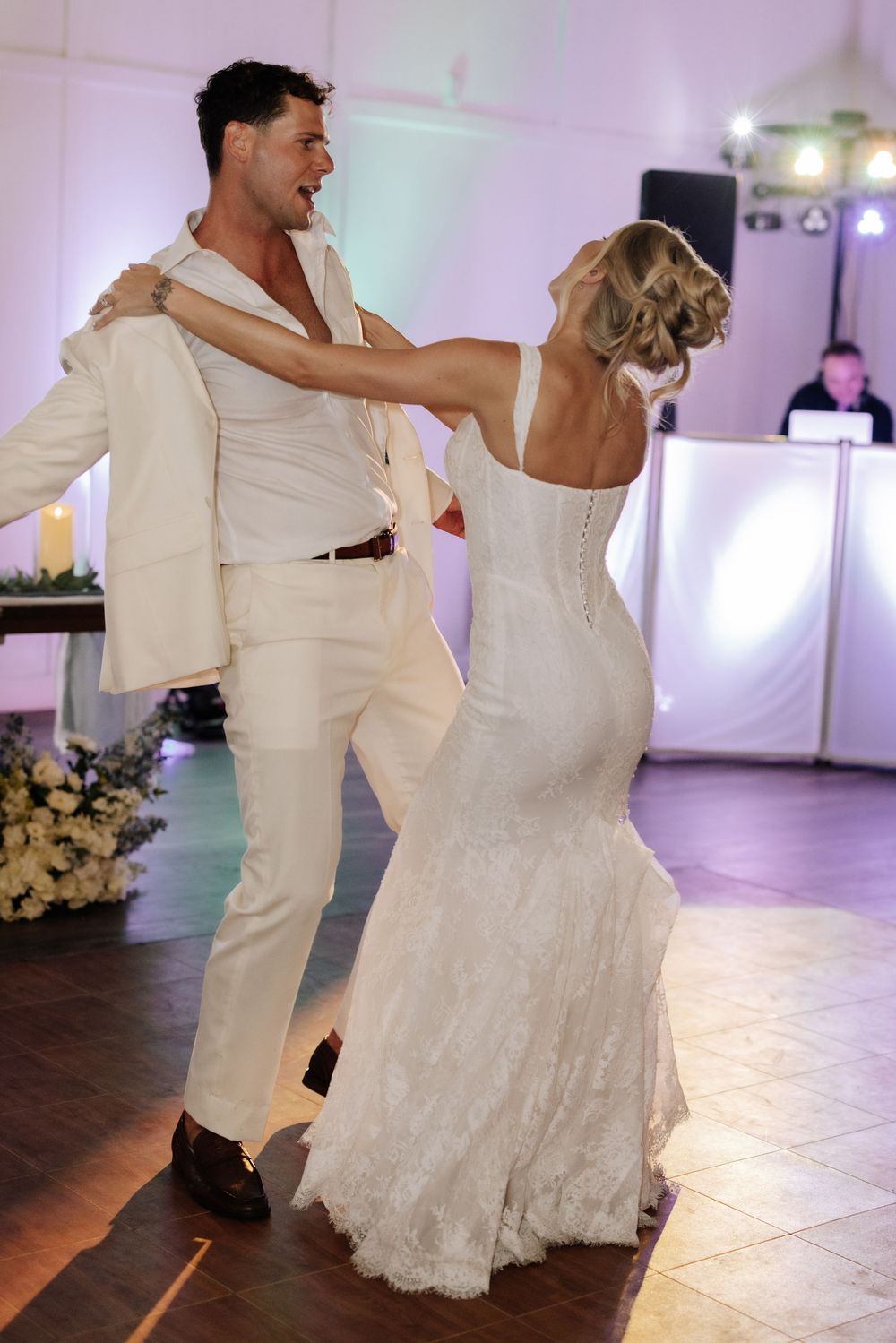 Bride and groom share their first dance at wedding reception, wearing white wedding attire.