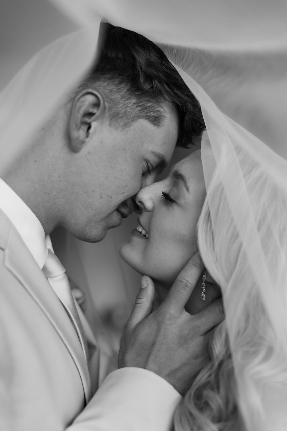 Black and white wedding photo of bride and groom sharing a romantic moment under a veil.