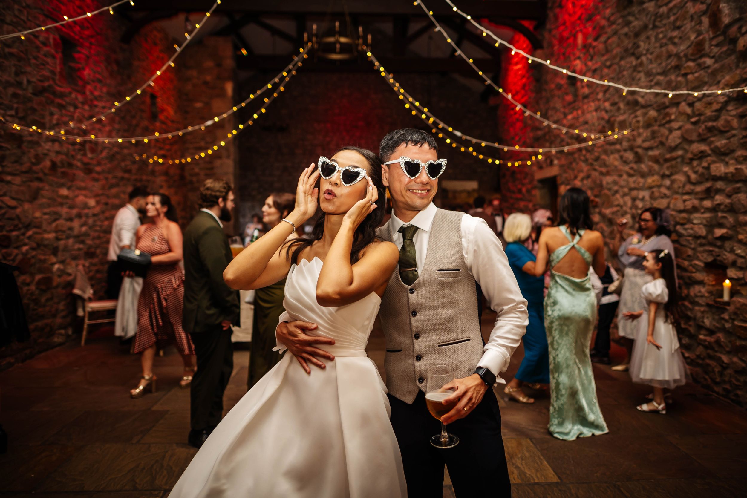 Bride & groom wearing sunglasses dancing at a wedding reception in a rustic barn with fairy lights at Browsholme Hall Wedding Venue