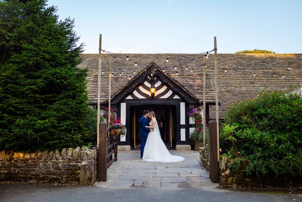 A stone-built barn entrance with timber-framed porch and tiled roof leading to a countryside wedding venue - Rivington Hall Barn Wedding