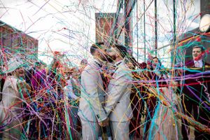 two grooms share a kiss during their confetti throw at the titanic hotel, Liverpool. guests are using paper streamers by Lynette Matthews