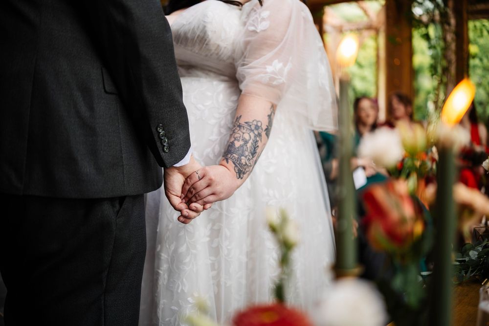 A close-up of a bride holding hands during a ceremony with a "The Lovers" tattoo by Lynette Matthews Photography at Oaktree of Peover