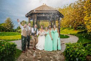 A wedding party gathers under a rustic wooden gazebo at Mytton Fold Wedding Venue, creating a champagne spray