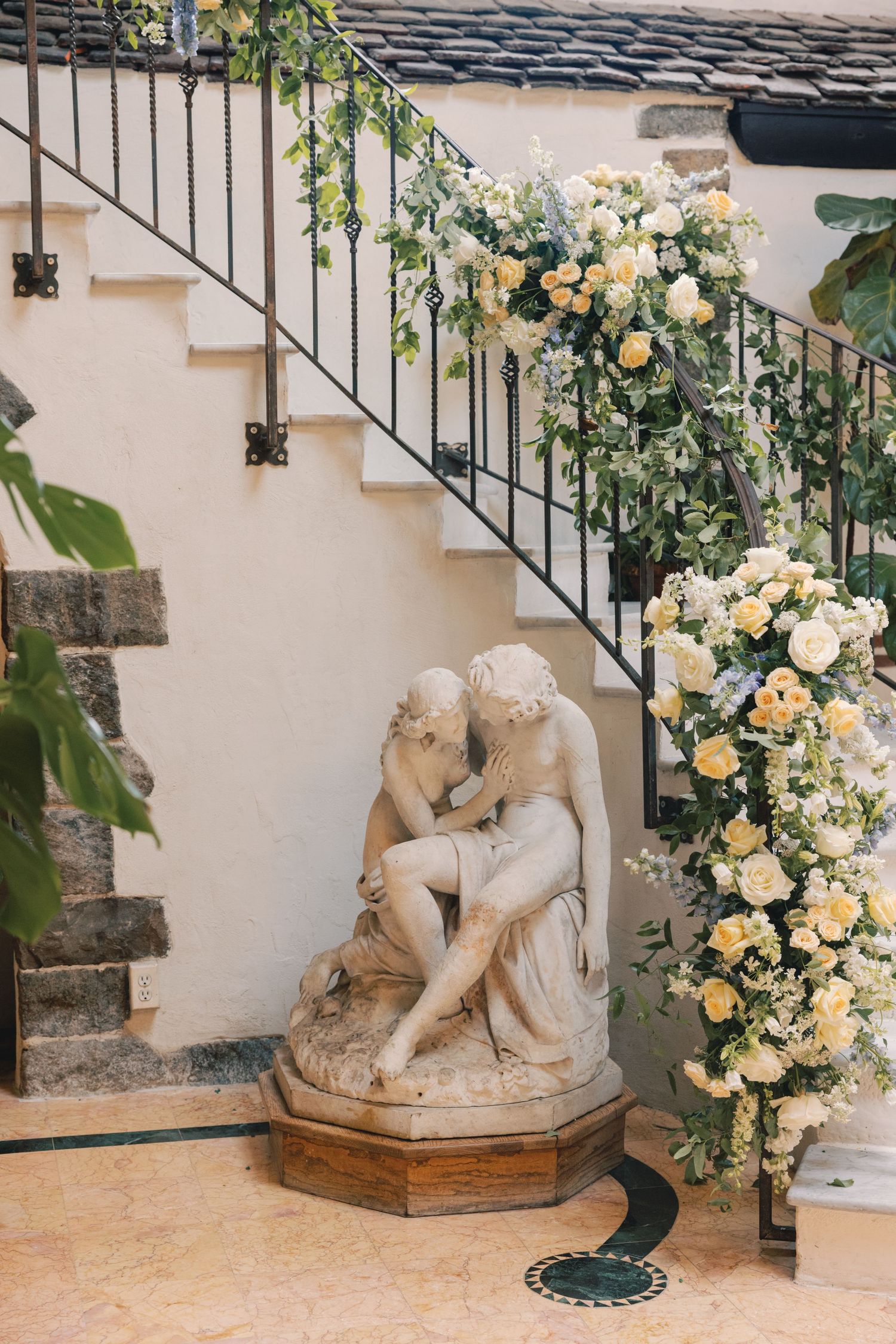 Classical marble sculpture beside a staircase adorned with white and yellow floral arrangements.
