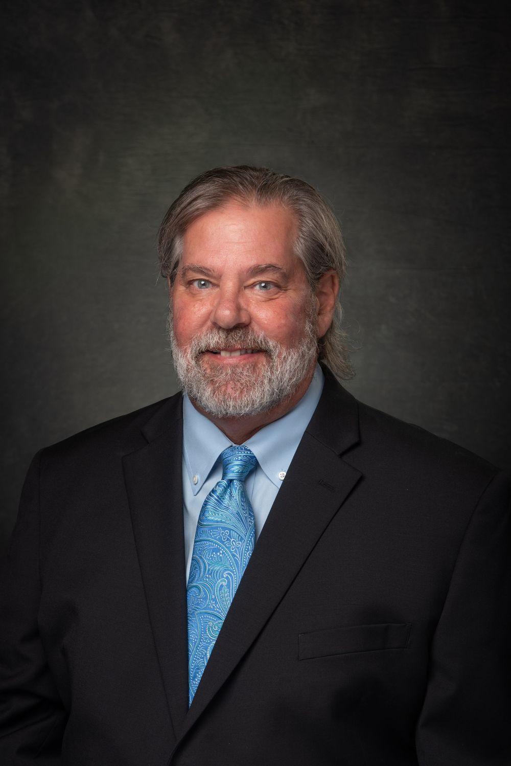 Headshot photo of bearded man in a suit with blue tie.